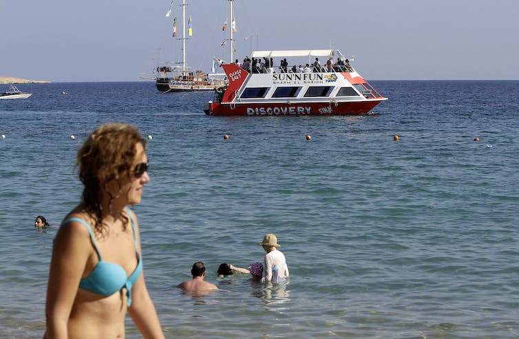 Une femme en maillot de bain devant la mer, avec un bateau en arrière-plan
