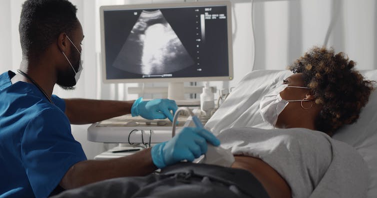 Médecin portant un masque de protection effectuant un dépistage par ultrasons pour une femme enceinte dans une clinique moderne