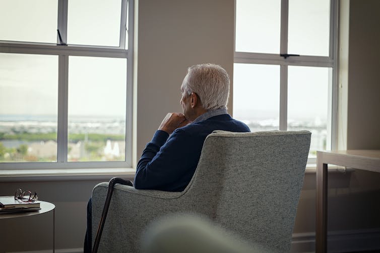 homme âgé assis sur un fauteuil regarde par la fenêtre