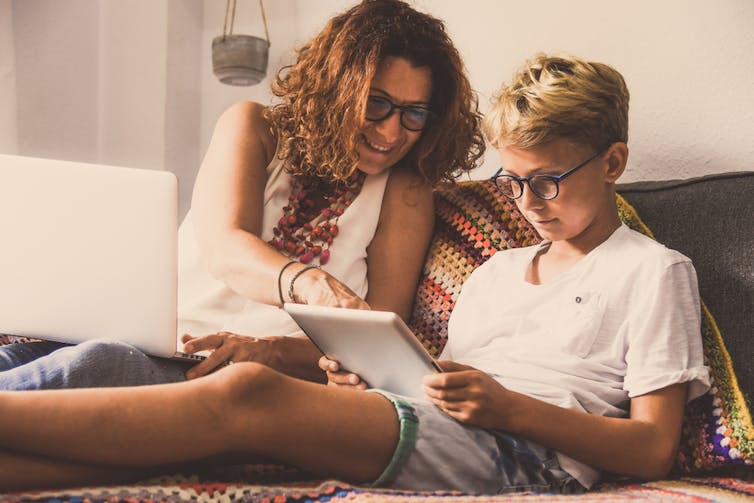 Bel adolescent lisant les nouvelles histoires tendance en ligne sur une tablette avec sa maman
