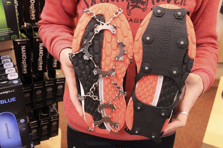 Image de la partie inférieure d’une paire de chaussures à semelle orange, présentant deux types de crampons à glace externes