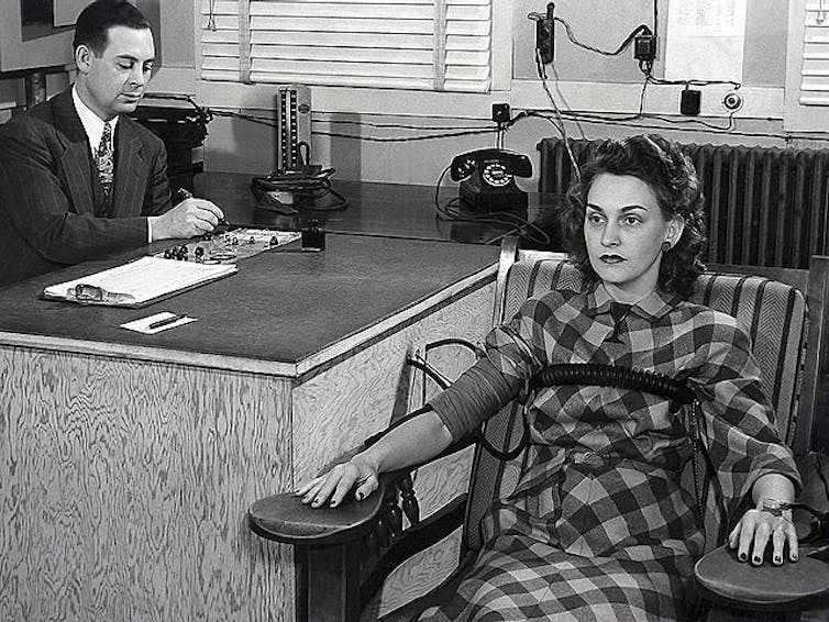 Photo d’un homme en costume assis à un bureau faisant passer un test polygraphique à une femme en robe