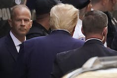 L’arrière de la tête d’un homme aux cheveux blonds est vue à l’entrée d’un tribunal