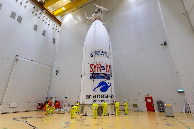 la coiffe contenant les satellites dans un hangar avec des travailleurs en tenues fluo