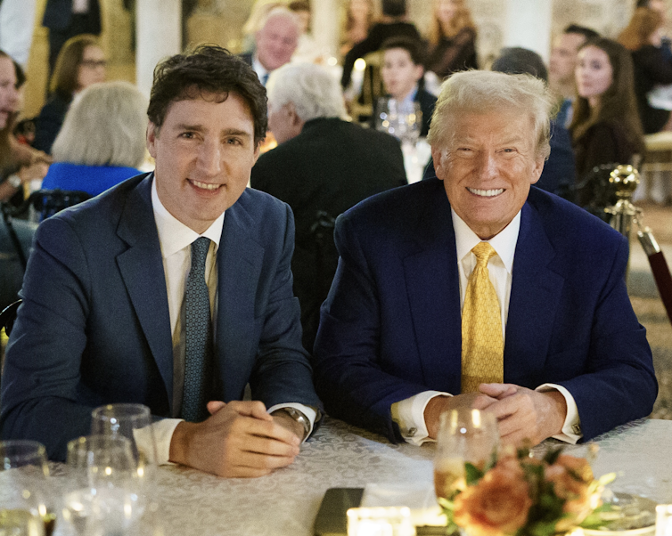 Un homme brun et un homme plus âgé aux cheveux blond-gris sourient à une table