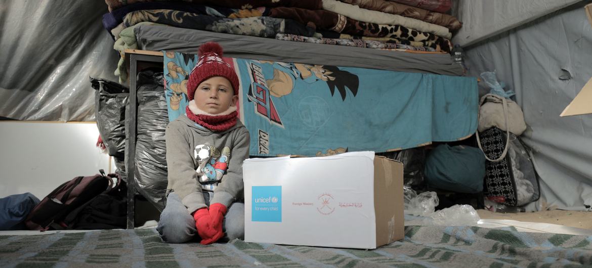 Un enfant à Gaza est assis à côté d'une boîte de vêtements d'hiver chauds fournie par l'UNICEF.