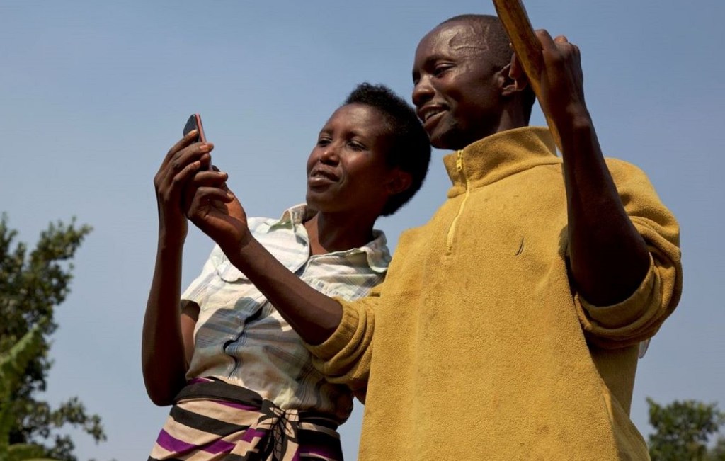 Deux agricultrices au Rwanda regardent untéléphone portable, grâce auquel elles reçoivent des bulletins météorologiques.