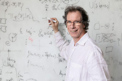 Portrait de Stéphane Mallat devant un tableau blanc couvert de formules mathématiques