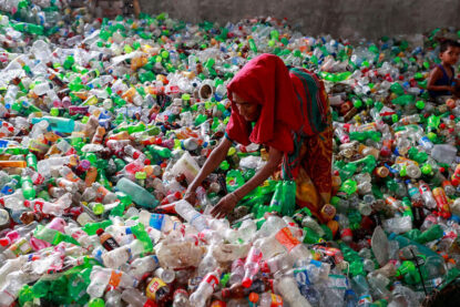 Une femme trie des bouteilles en plastique avant leur recyclage, son enfant en arrière-plan sur l’amoncellement de bouteilles
