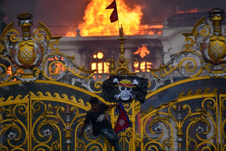 Le « jolly roger », pavillon noir de l’équipage des chapeaux de paille dans One Piece devant un bâtiment en flammes