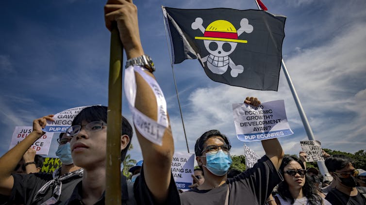 Des manifestants, dont certains portent des masques, brandissent un drapeau représentant un crâne coiffé d’un chapeau de paille