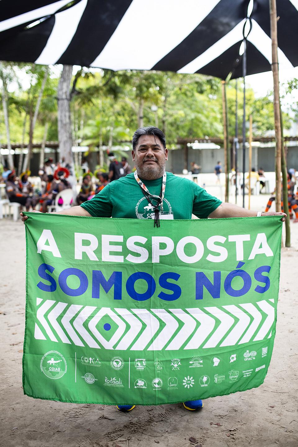 Un homme debout en t-shirt vert tient une banderole sur laquelle il est écrit « A resposta somos nos ».