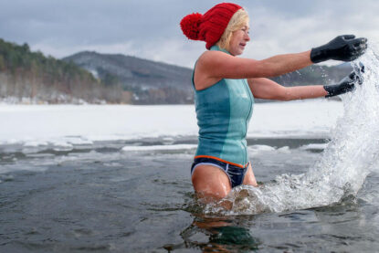 Une femme avec des gants et un bonnet rouge se baignant dans un lac gelé