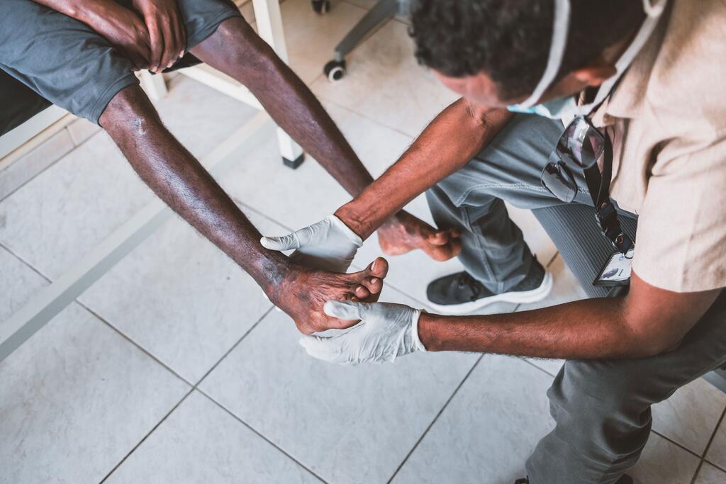 Un travailleur médical portant des gants examine le pied blessé d'un migrant africain assis dans une clinique.